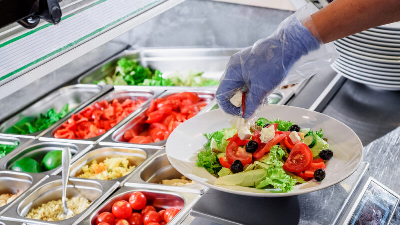 Chef prepares salad at the salad bar. Salad making process. Showcase salad bar with an assortment of ingredients for healthy and dietary food. High quality photo
